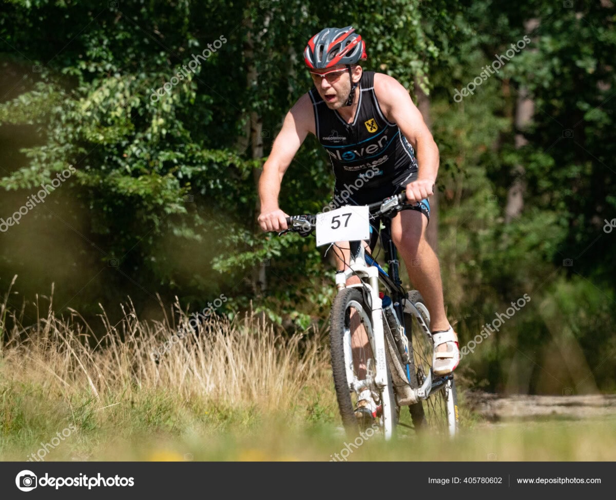 mtb bikers racing along on rural road metween meadow and forest